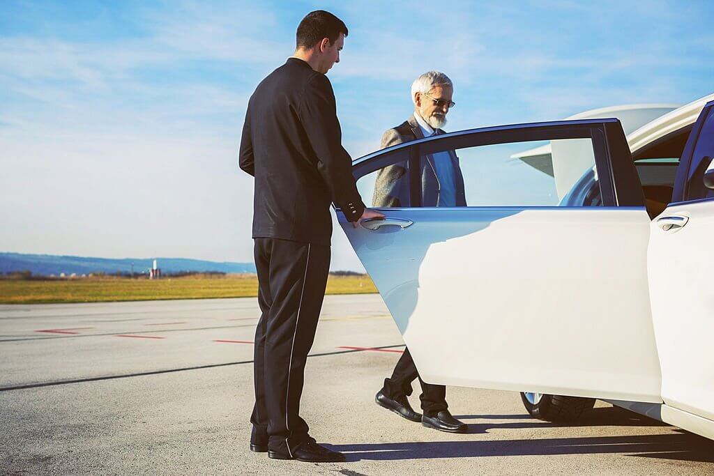 Driver helping senior adult into limousine at airport.