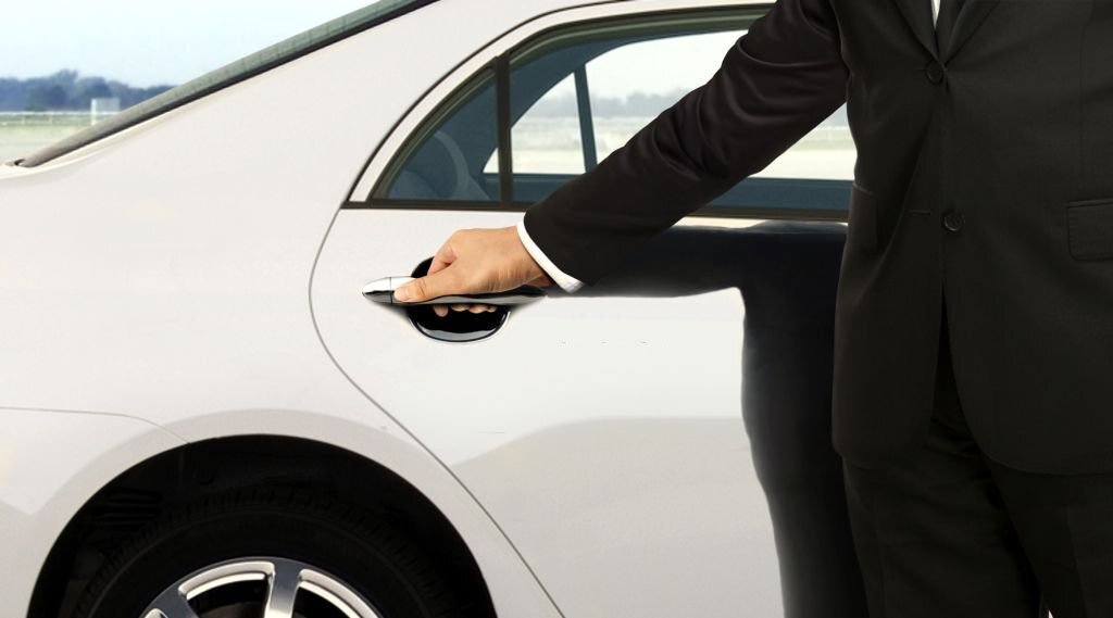 Driver in black suit opening white car door