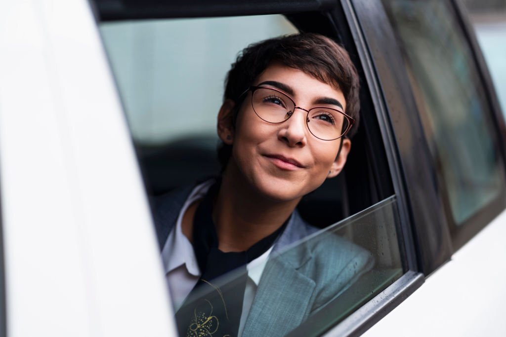 Smiling young Caucasian businesswoman looking out of a car window.