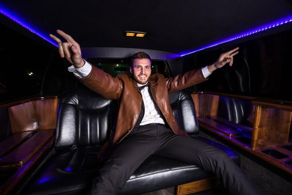 A man wearing a brown leather jacket sits in the back of a limo, 