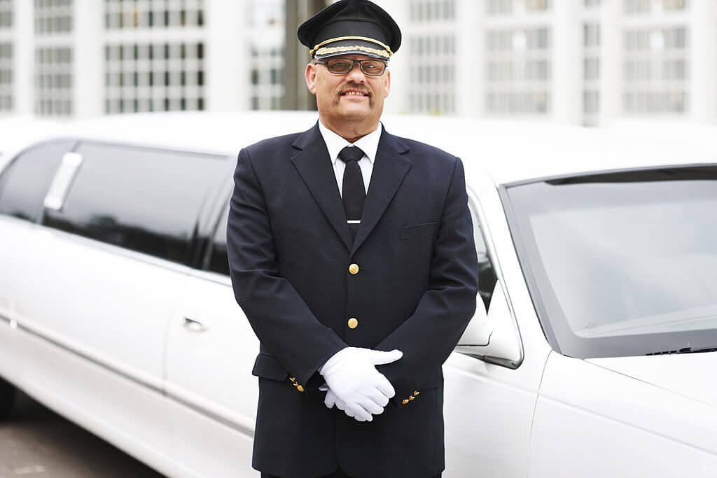 Portrait of a proud chauffeur standing beside a white stretch limousine